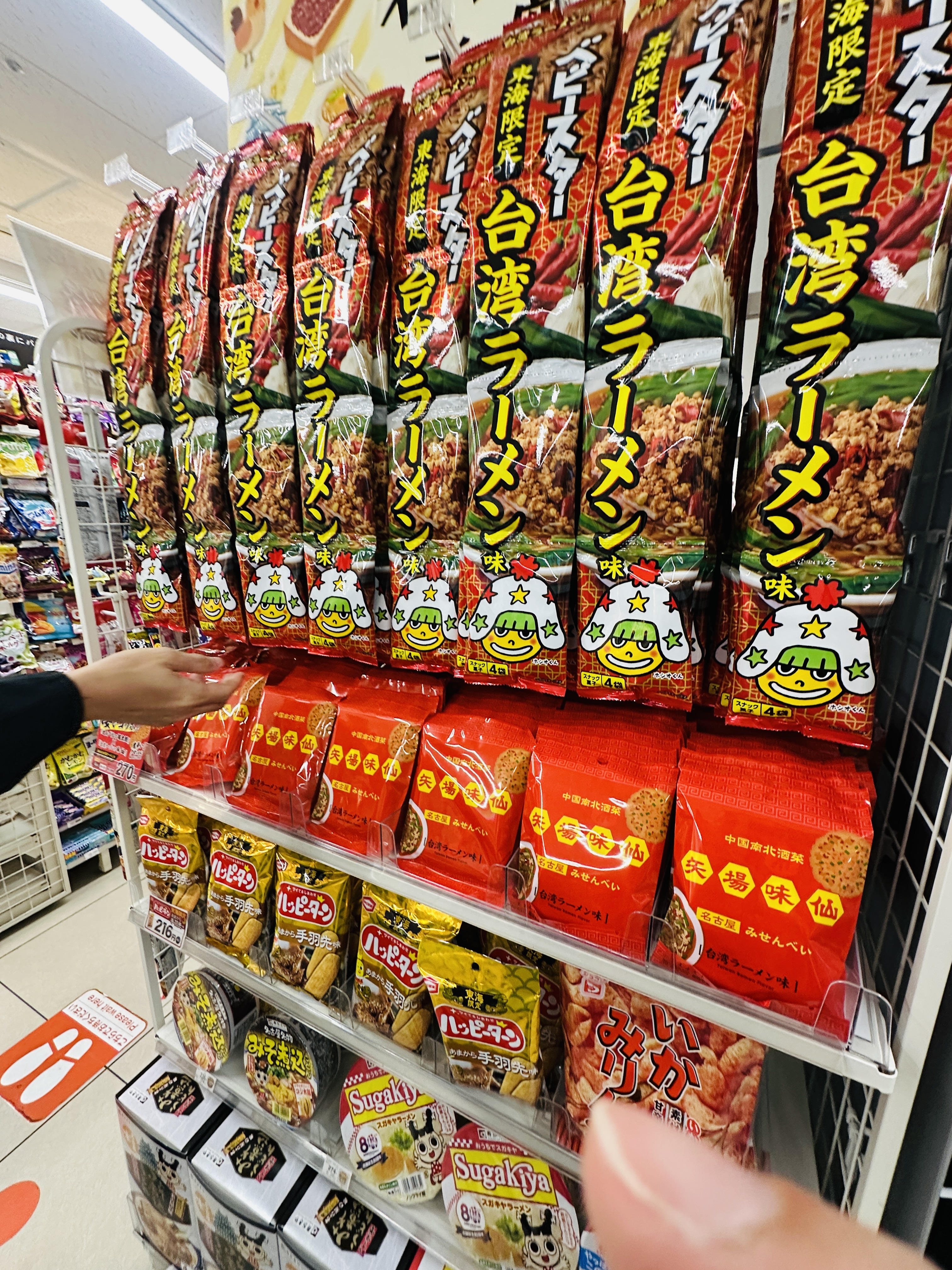 超市貨架上一整排「台灣拉麵」泡麵，紅色包裝上印著卡通娃娃圖案，下層是紅色包裝的餅乾