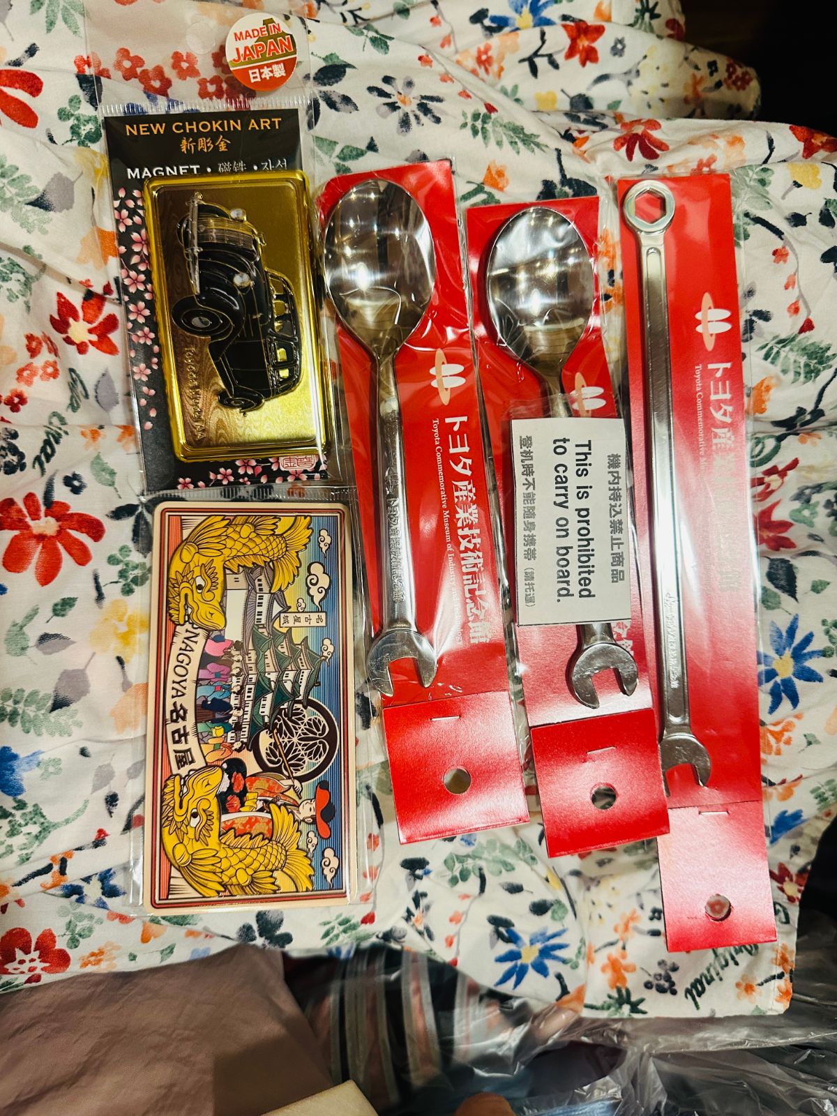 買回來的紀念品攤在花布上，有老爺車造型的磁鐵、名古屋圖案的鐵盒，以及兩支湯匙與兩支扳手造型的餐具
