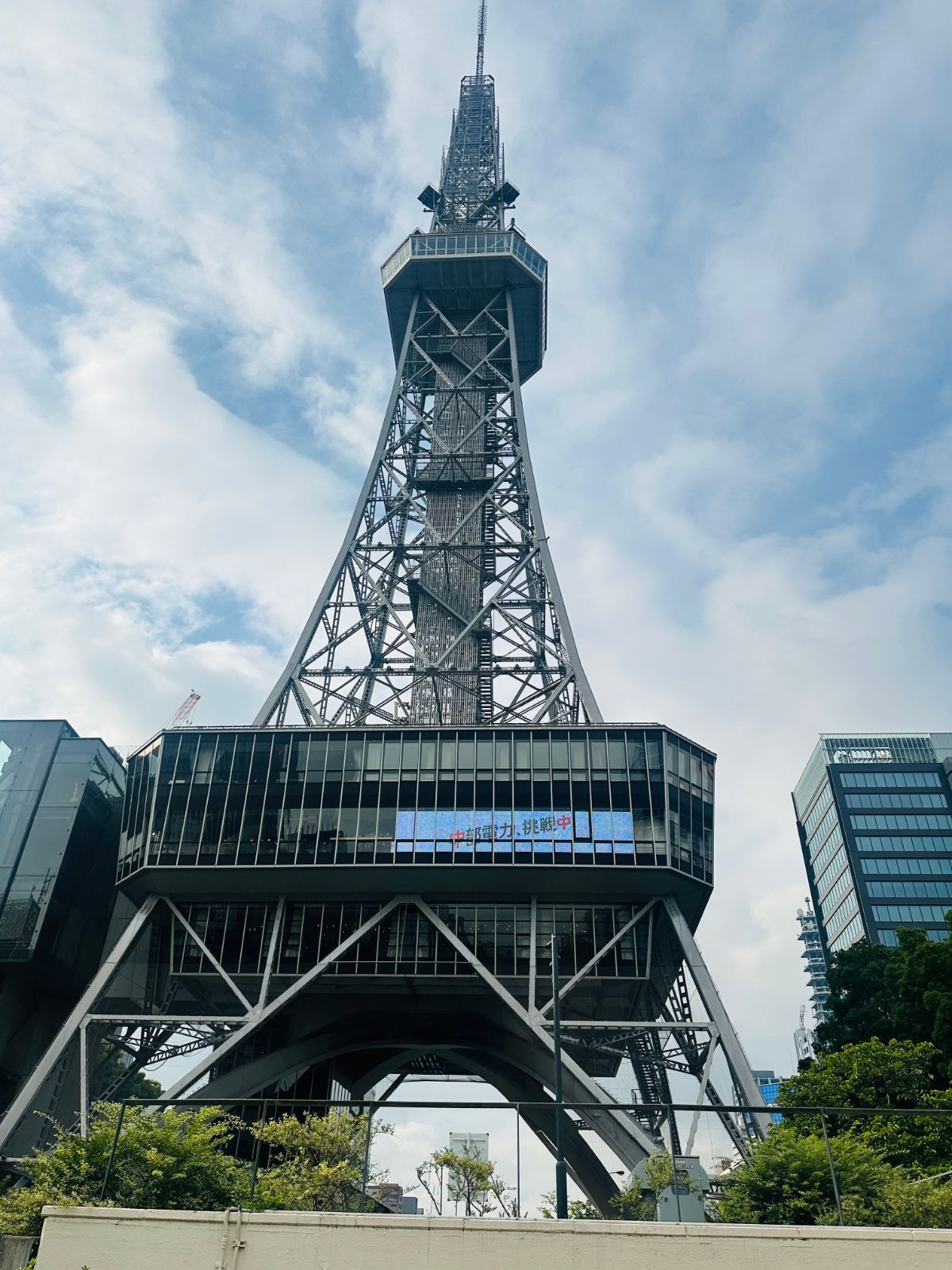 仰角拍攝的中部電力 MIRAI TOWER，鋼構塔身直入多雲的天空，中段是玻璃帷幕的展望台