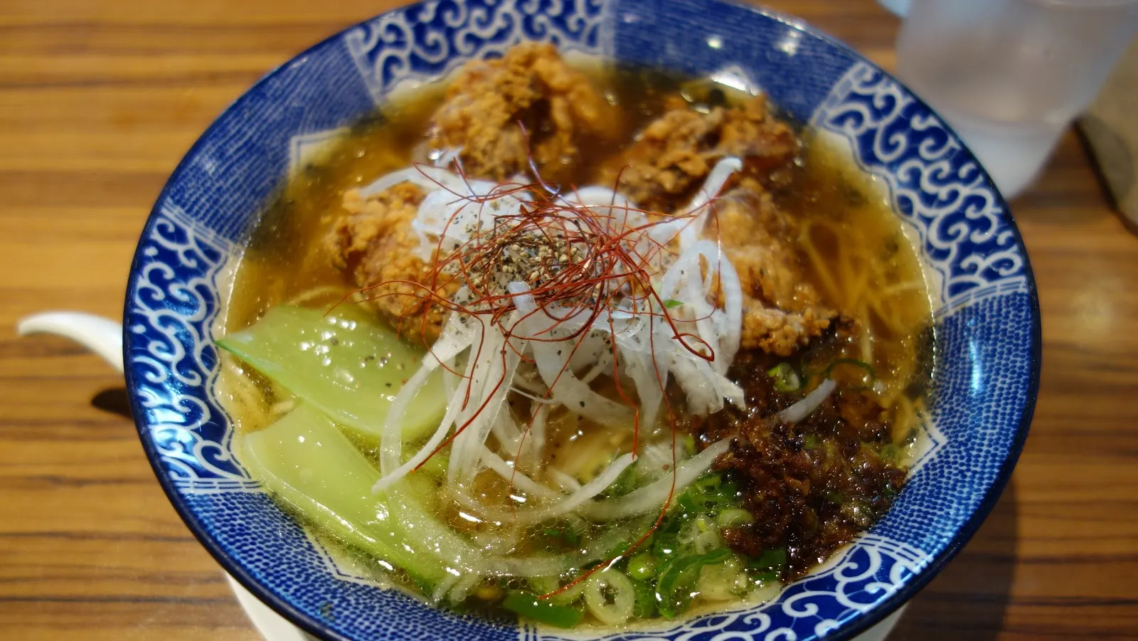 藍白花紋的大碗裡是炸雞拉麵，湯上鋪著炸雞塊、白蔥絲、辣椒絲與青江菜