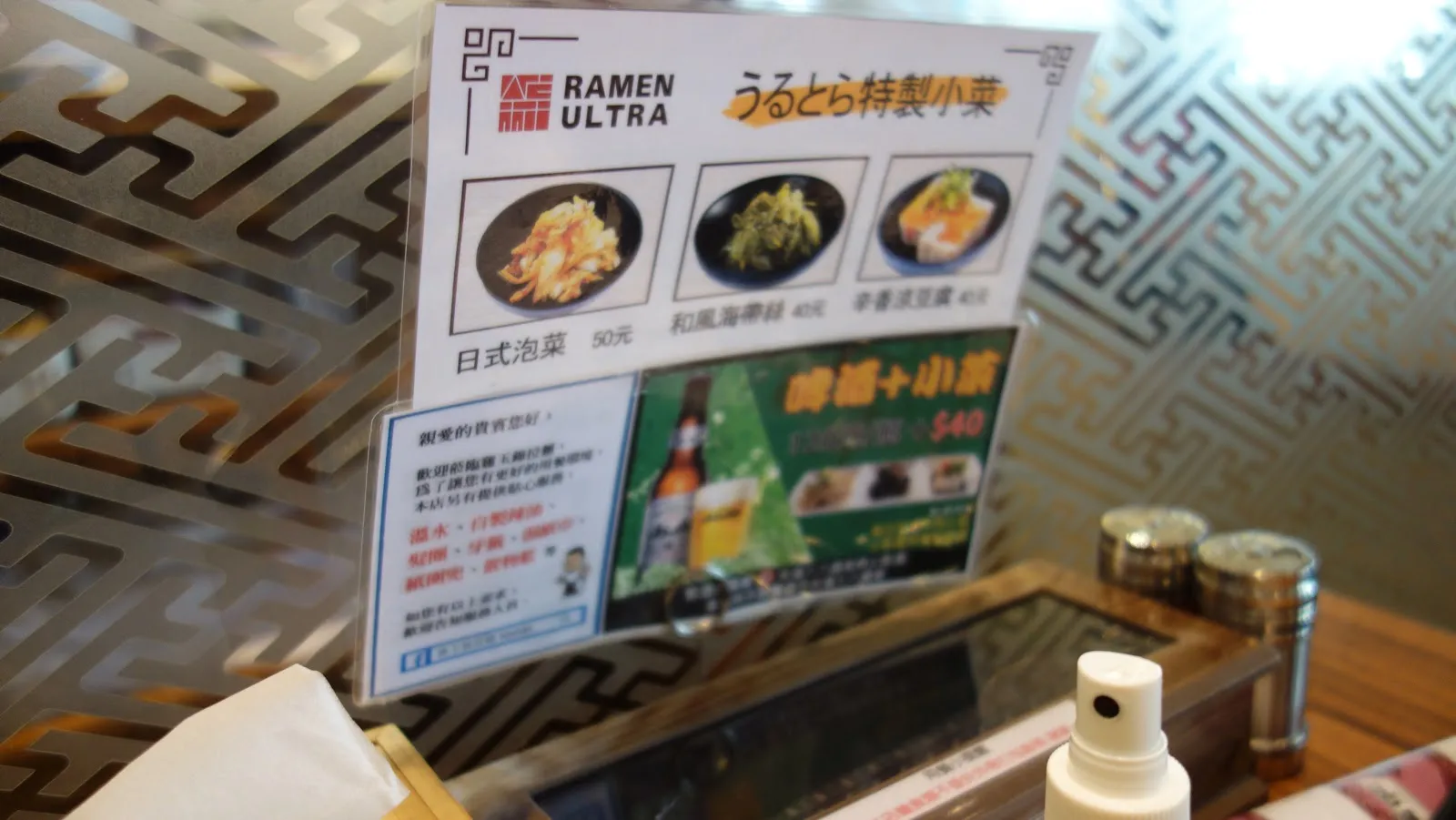 桌上立著「うるとら特製小菜」的桌卡，介紹日式泡菜、和風海帶根與辛香蔥花，下方是晚間加點小菜 40 元的優惠，旁邊放著調味料瓶