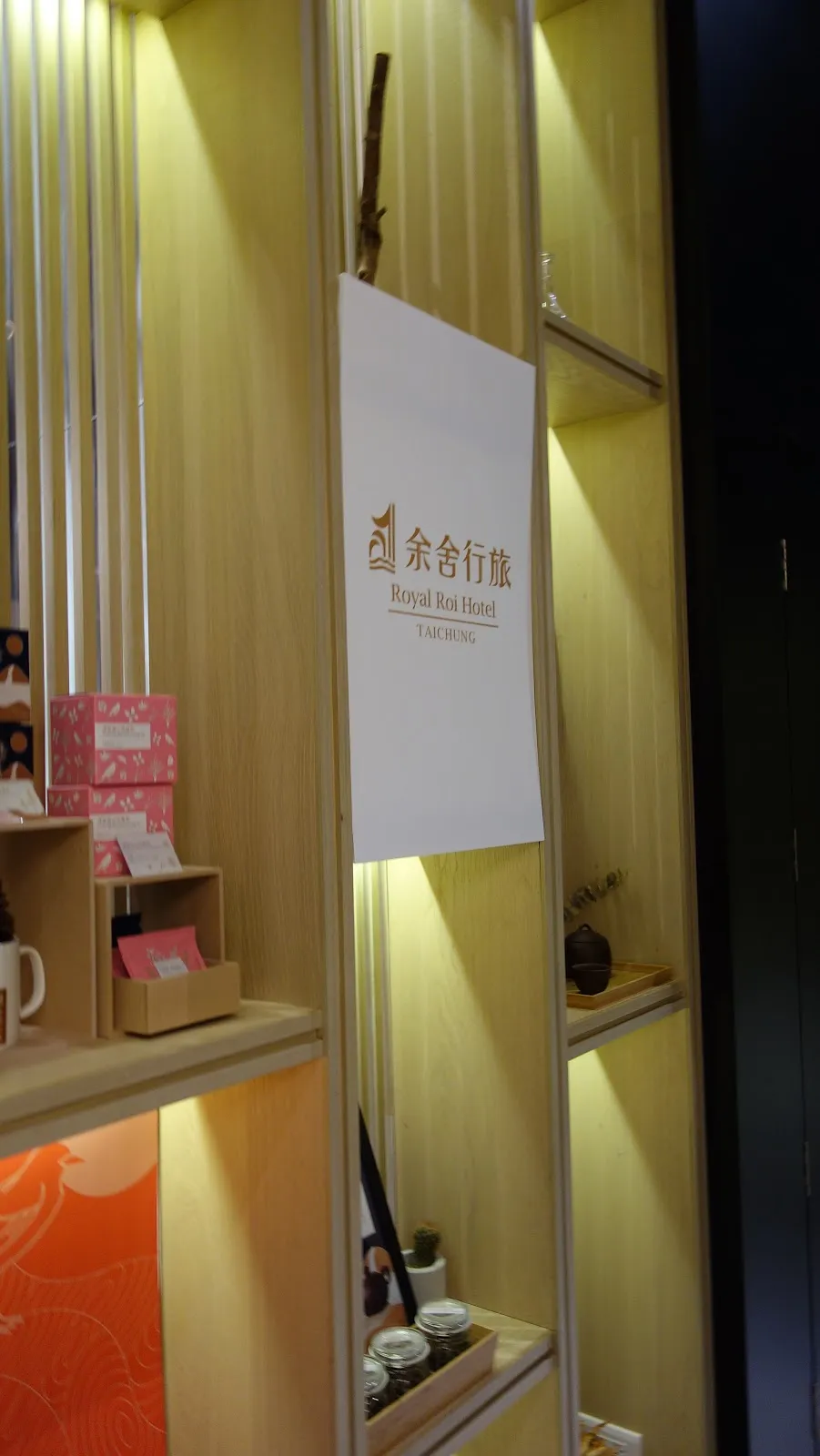 飯店大廳的展示櫃，燈光打在木質層架上，中央立著余舍行旅的白色立牌，架上擺著杯具與伴手禮