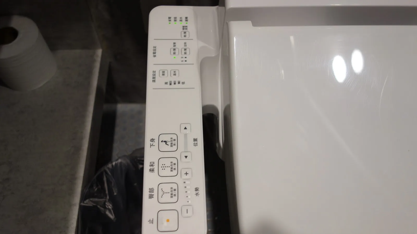 免治馬桶的操作面板，白色按鍵標示著各種沖洗功能，旁邊放著捲筒衛生紙