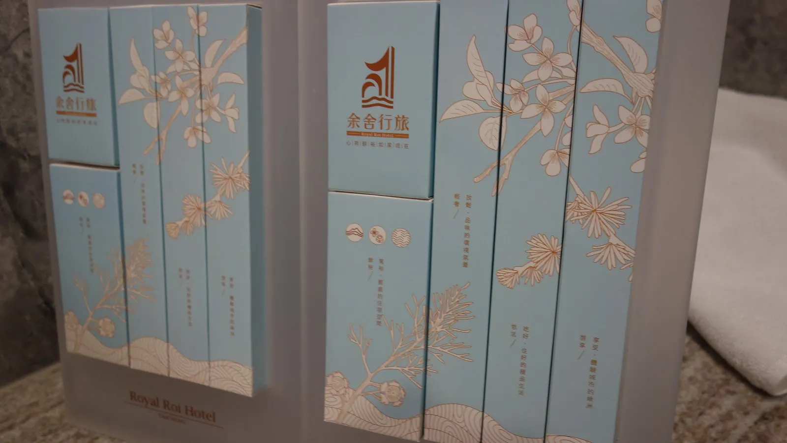 淺藍色包裝的伴手禮盒並排立在架上，盒面印著余舍行旅的金色標誌與花草圖案