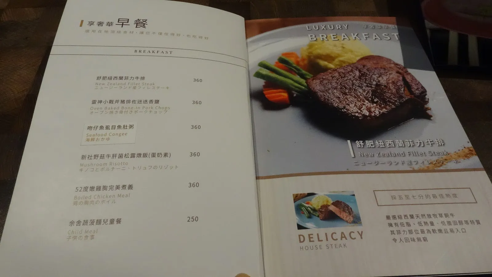 攤開的早餐菜單，左頁列出六道主餐 250 到 360 元，右頁是牛排主餐的照片與 DELICACY 標題