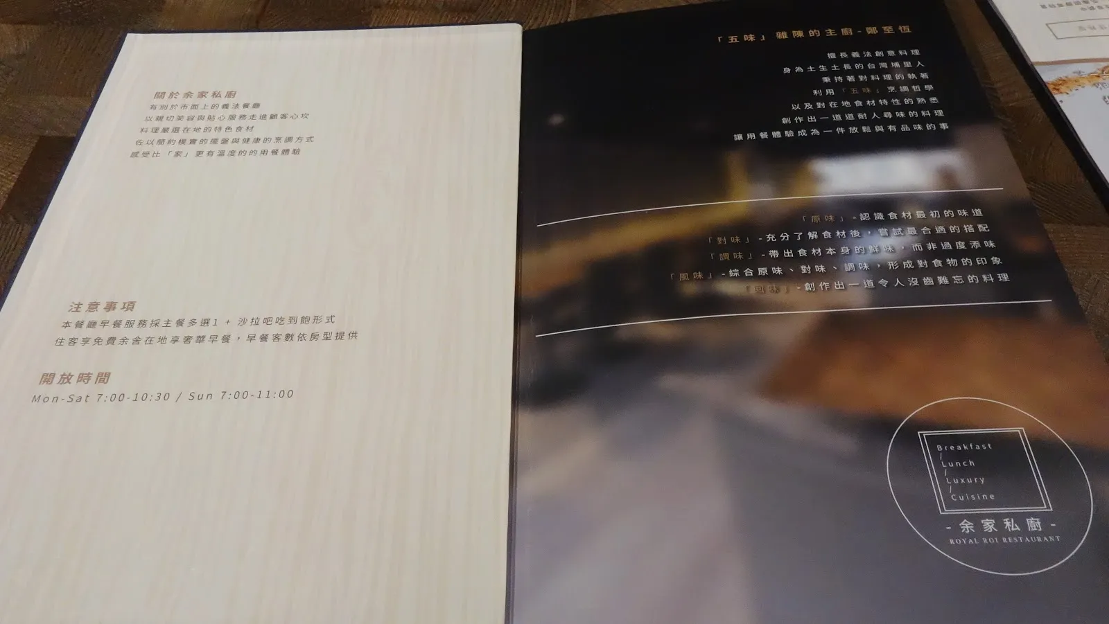 桌上攤開的說明卡，左頁是白紙黑字的注意事項與供餐時間，右頁是深色的餐廳形象照