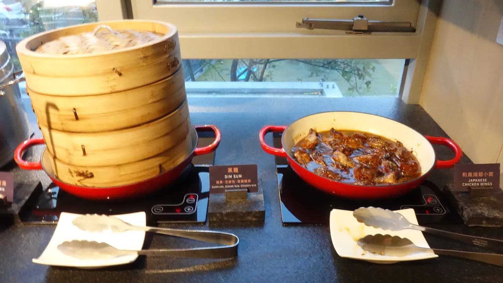 熱食區，竹製蒸籠與紅色鑄鐵鍋並排放在保溫爐上，前方擺著夾子與餐盤