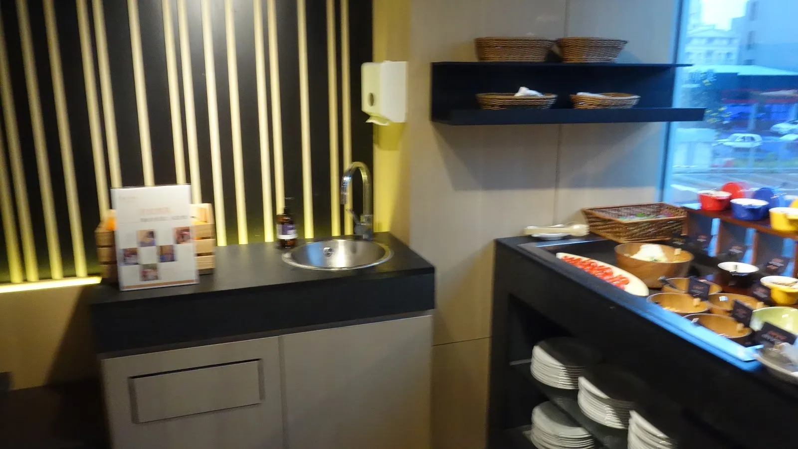 餐廳一角的取餐檯，小水槽旁堆著白色餐盤，牆上是暖黃燈光的木格柵