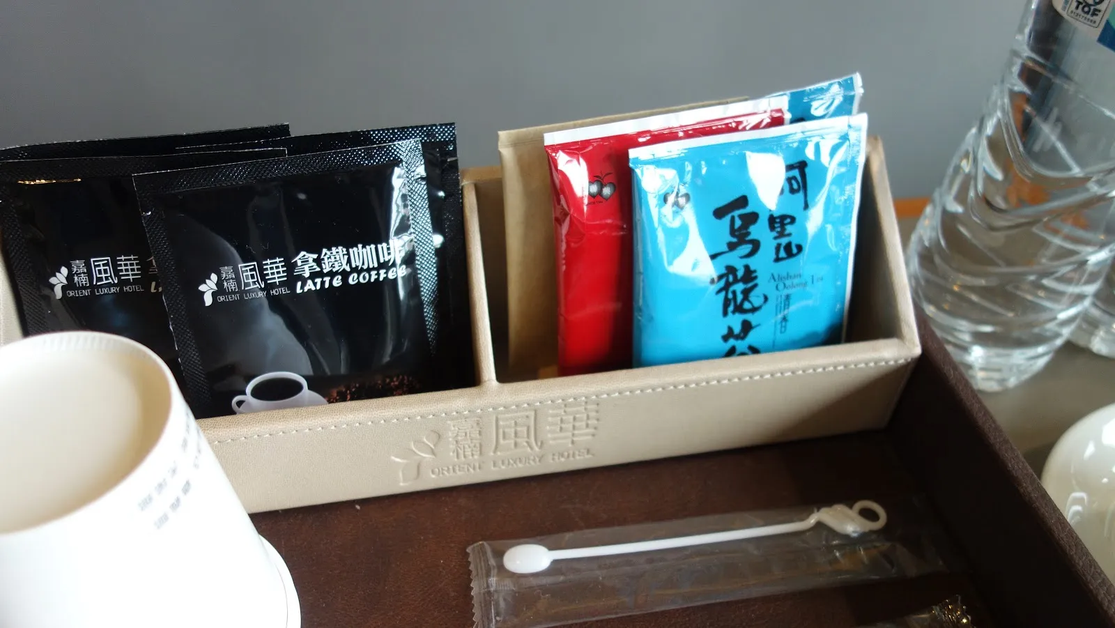 房內的茶水區，木盒裡放著拿鐵咖啡包與烏龍茶包，旁邊是白色馬克杯與礦泉水