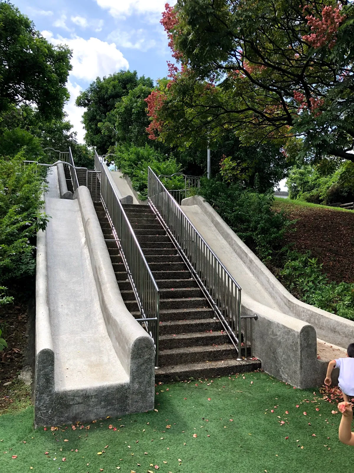 公園的兩道磨石子溜滑梯，中間夾著階梯，滑道下方鋪著綠色人工草皮