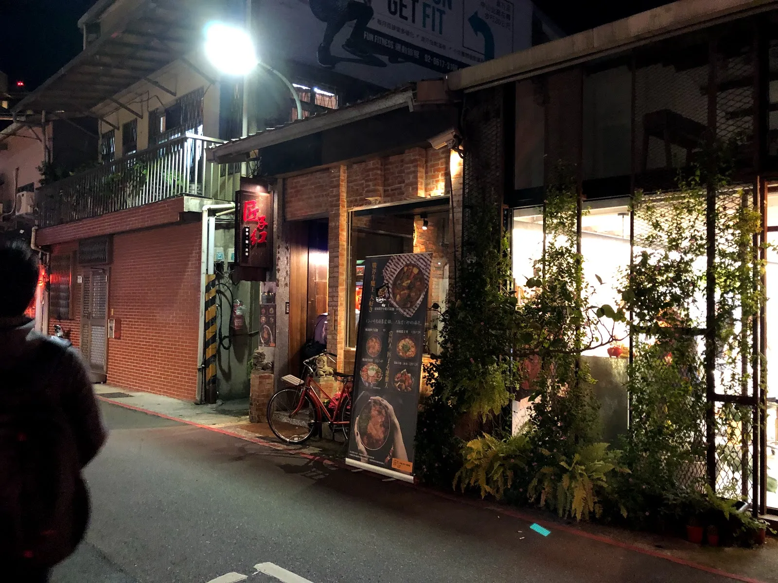 夜晚的巷弄街景，一整排店家的燈光映在路面上，門口擺著盆栽