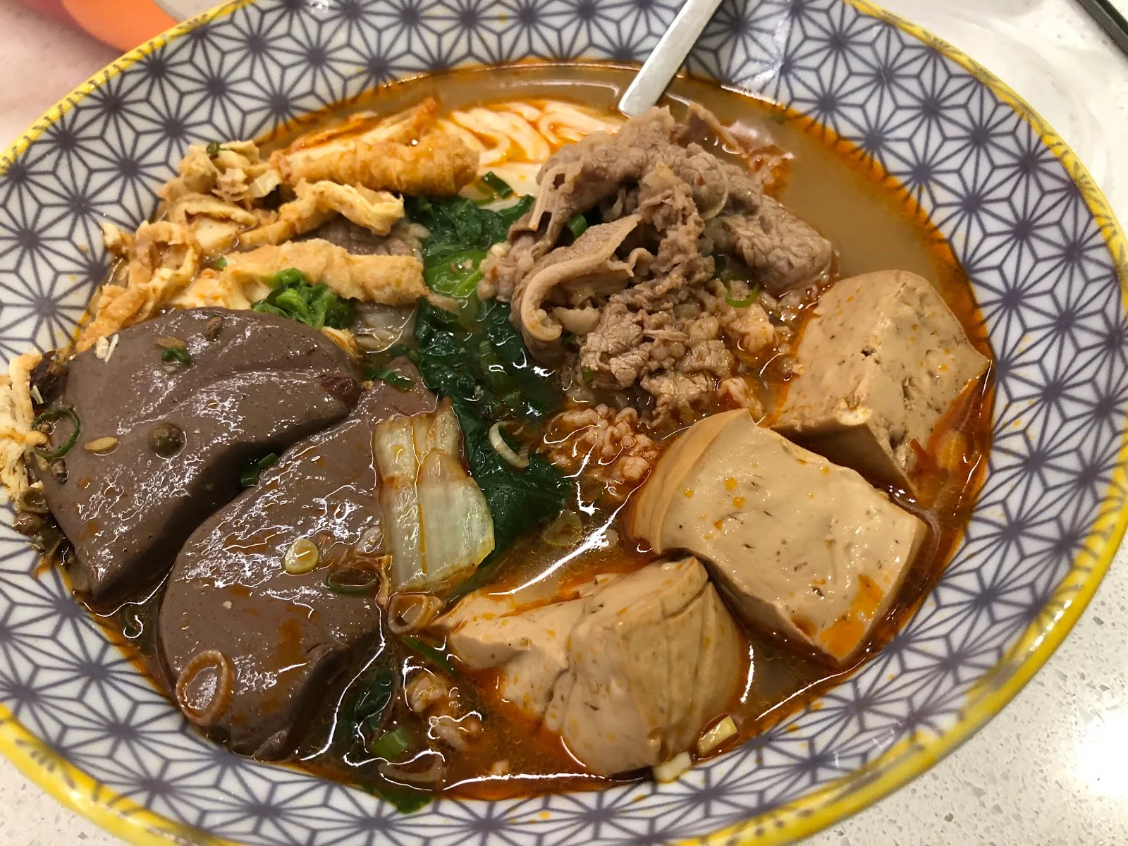 幾何花紋的碗裡是麻辣豆腐鴨血湯麵，湯裡有鴨血、豆腐、肉片、青菜與豆皮