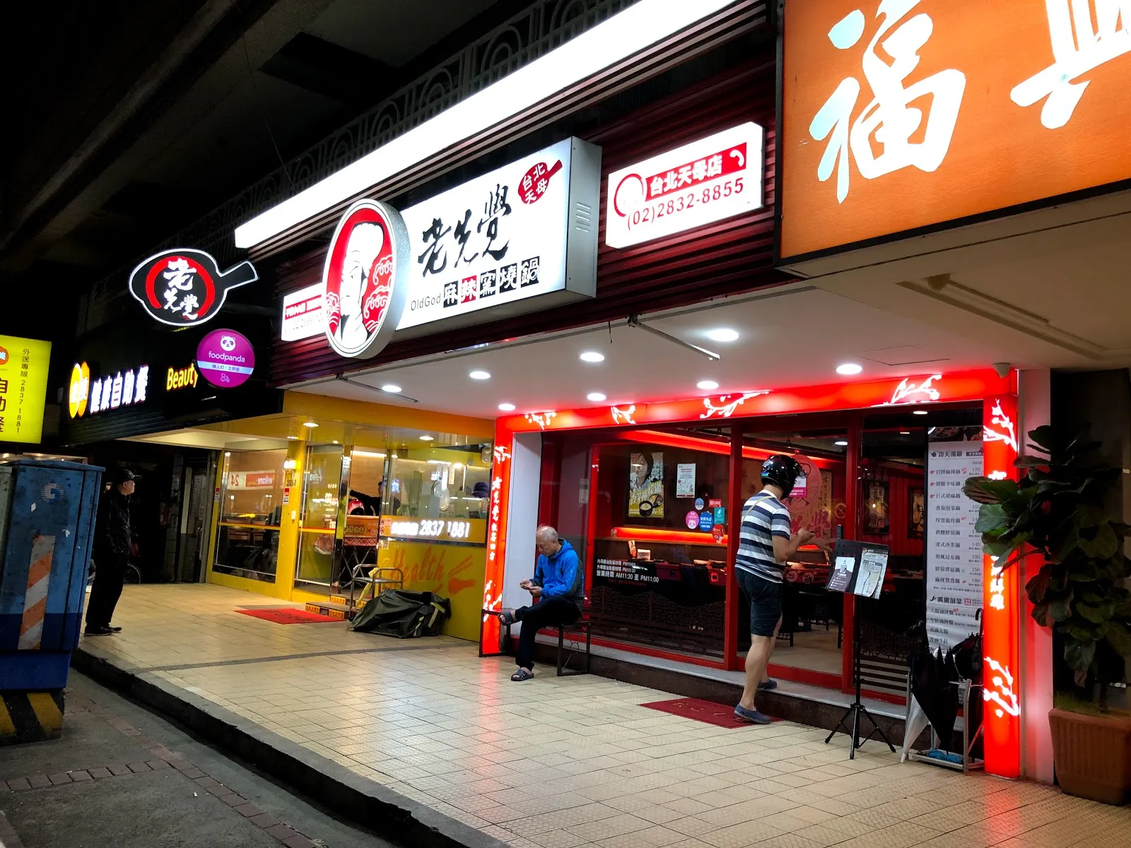 老先覺的店門外觀，夜裡紅色招牌亮著燈，旁邊是另一家店的黃色招牌，門口站著客人