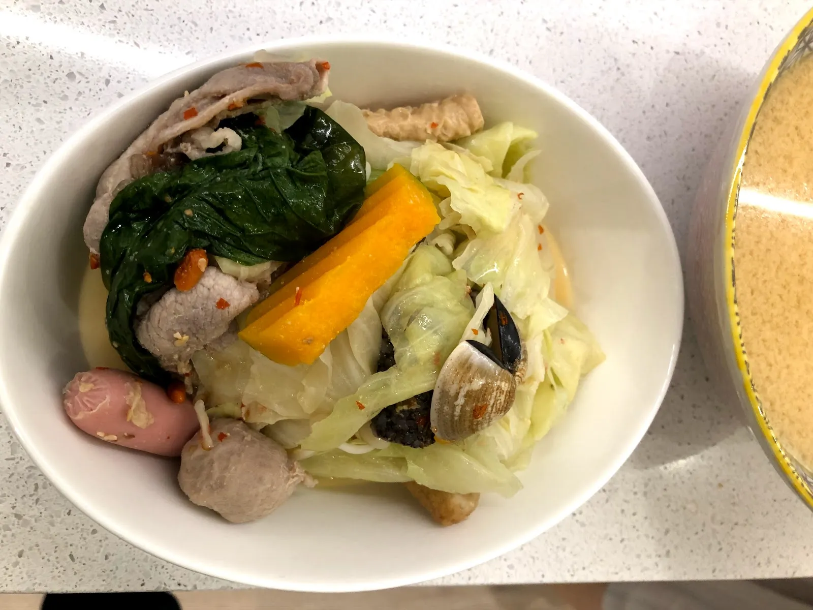 白碗裡的鍋料，有肉片、青菜、南瓜、香腸與貢丸，旁邊是一碗湯