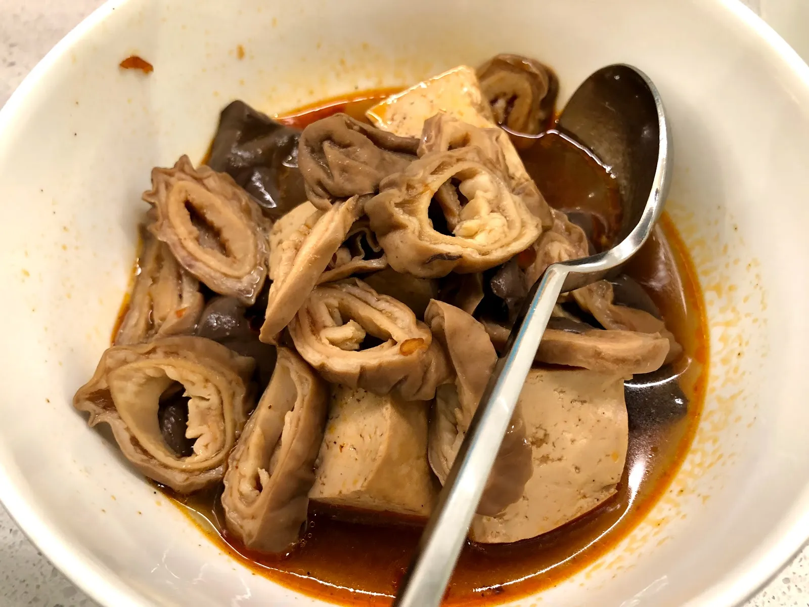 白碗裡的麻辣大腸與豆腐，滷得軟嫩的腸段泡在紅油湯裡，插著一支湯匙
