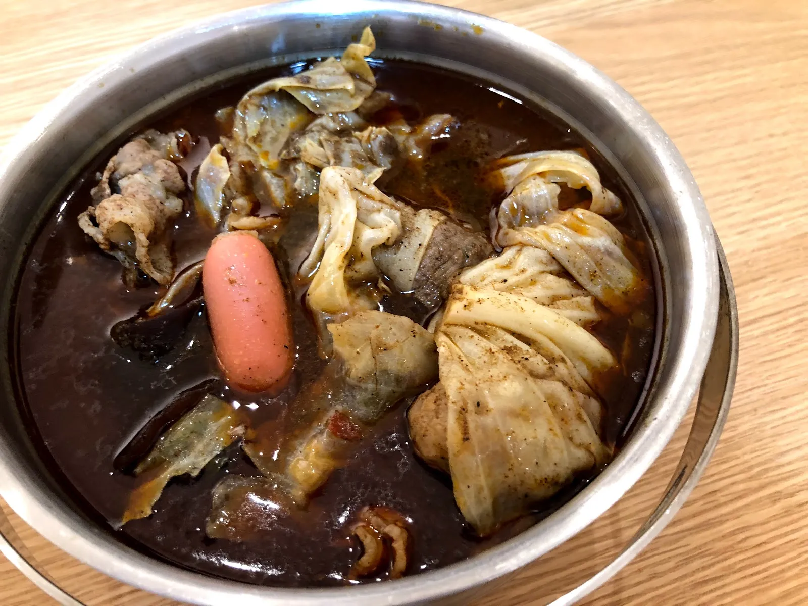 不鏽鋼鍋裡的麻辣鍋，深色湯裡有肉片、豆皮、香腸與高麗菜