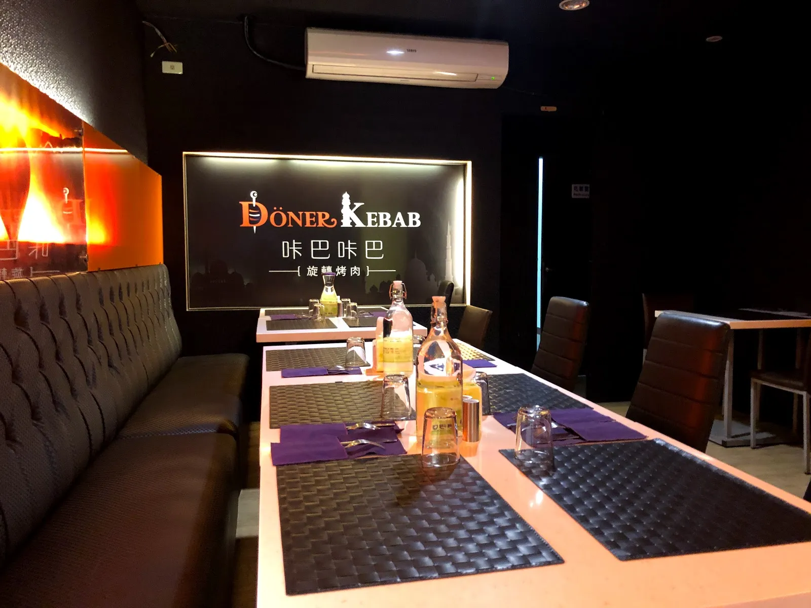 咔巴咔巴的店內，牆上是 DÖNER KEBAB 的燈牌，長桌配紫色餐墊與沙發座，旁邊立著旋轉烤肉爐