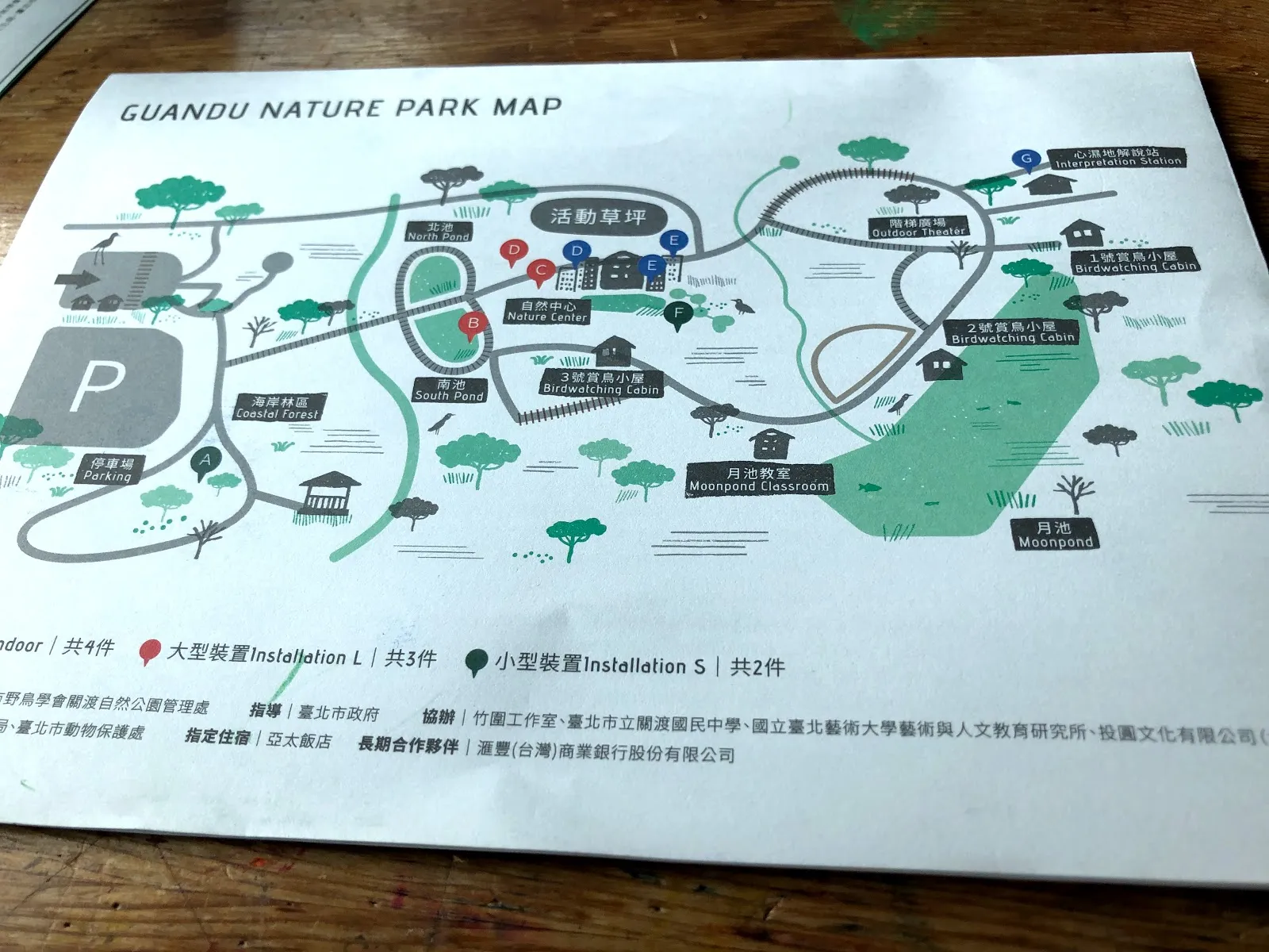 攤在木桌上的關渡自然公園地圖，綠色印刷的園區平面圖標示著停車場、賞鳥小屋與各展示區