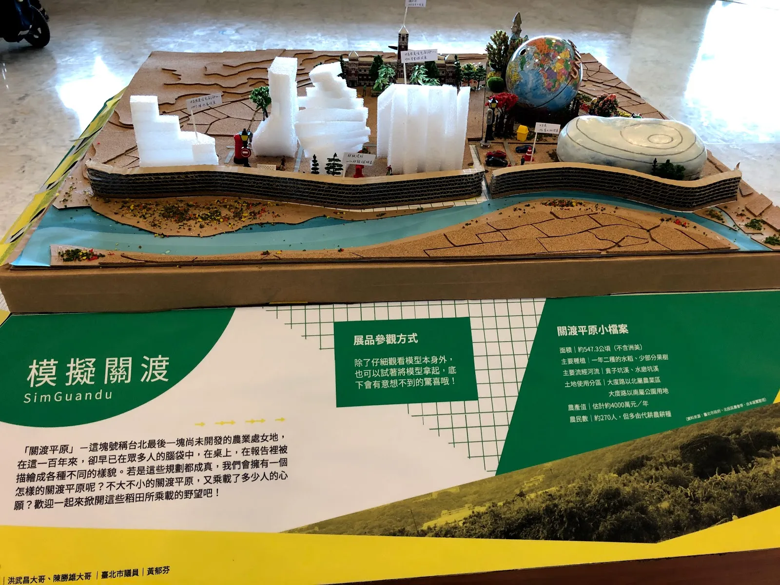 「模擬關渡」的立體模型展示，白色建築與地形模型架在木台上，前方是綠色的解說看板