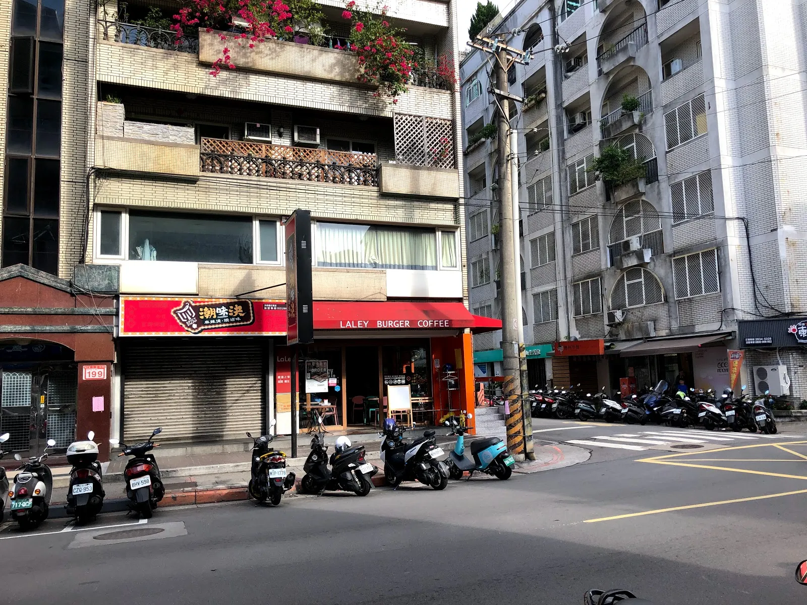 街角的 Laley Burger Coffee 店面，紅色招牌下是整面玻璃門窗，門口停滿機車