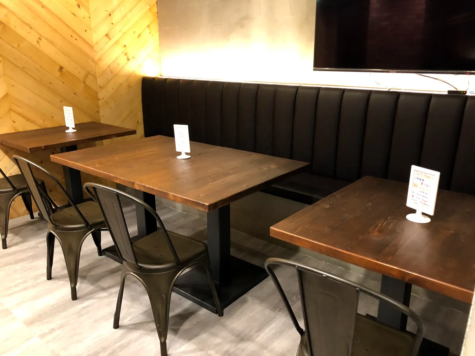店內用餐區，深色皮質長椅沿牆排開，配上木紋方桌與黑色鐵椅，牆面是木板拼接
