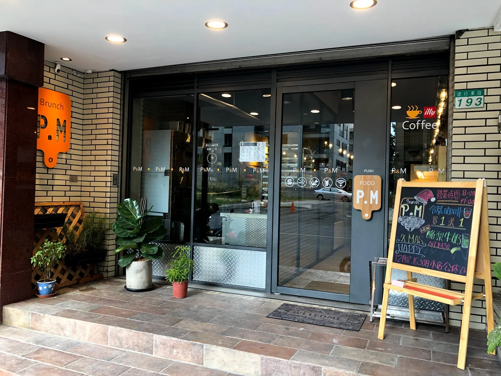 P.M Brunch 的店門口，灰色門面配橘色招牌，門邊立著木框黑板與盆栽