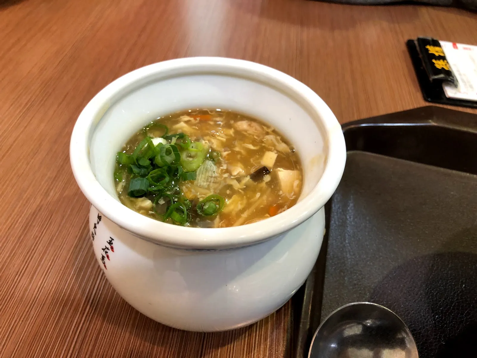 白色湯盅裡的酸辣湯，湯面撒滿蔥花