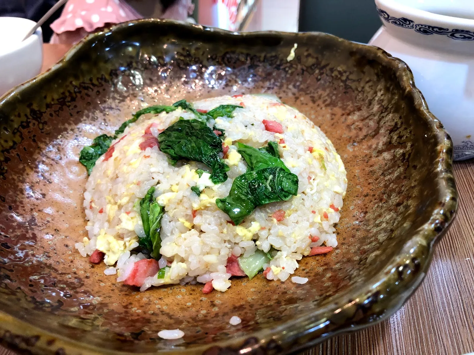 深色陶盤裡的青菜蛋炒飯，飯粒粒粒分明，拌著蔬菜與火腿丁