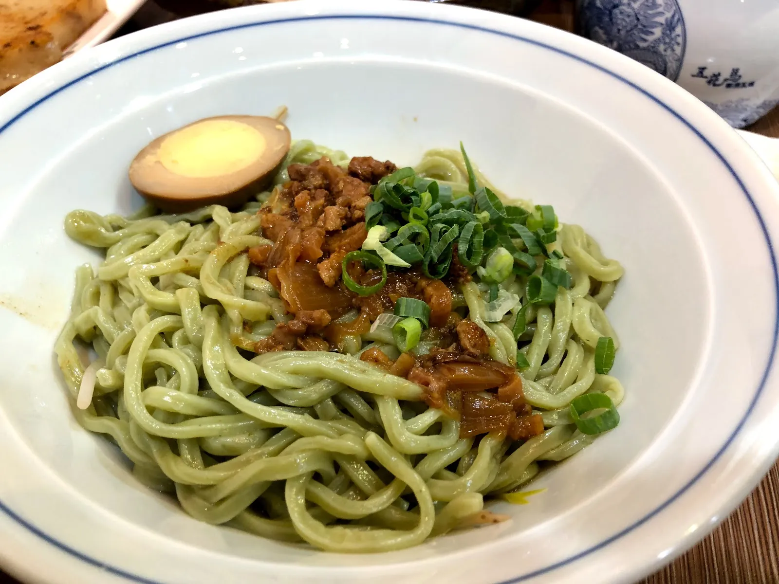 藍邊白盤裡的翠綠色麵條，鋪著肉燥、蔥花與半顆滷蛋