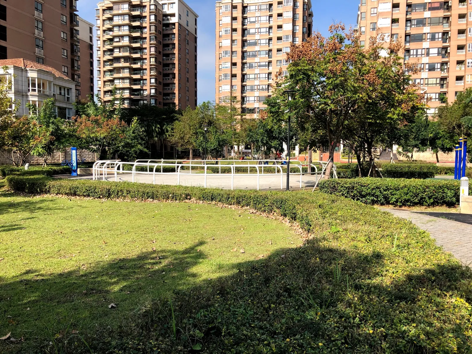 公園的草坡與步道，遠方是一整排公寓大樓與白色的休憩設施