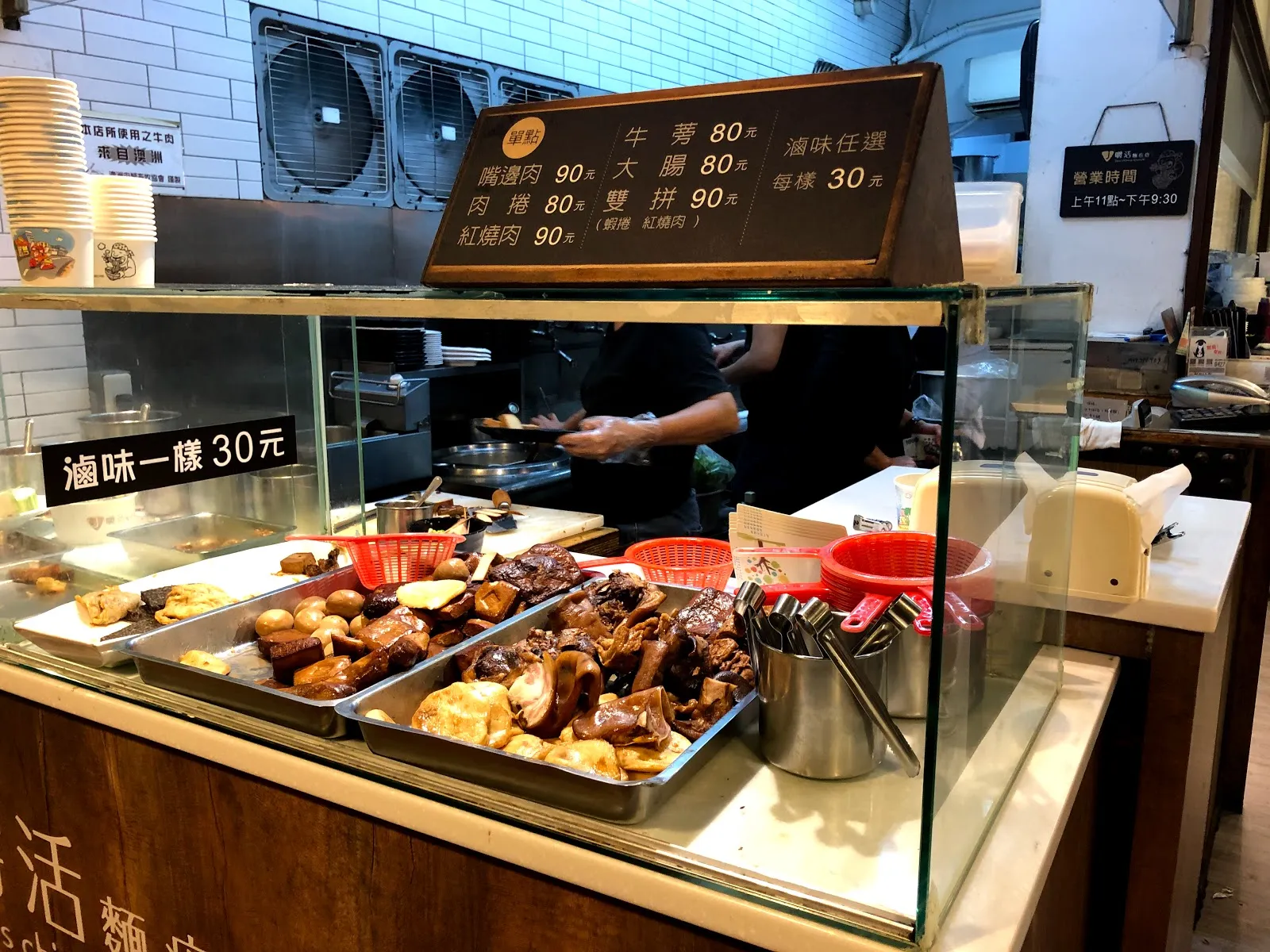 店家的點餐櫃檯，玻璃櫃裡是滷味與小菜的分格鐵盤，上方燈箱菜單寫著牛肉 80 元、雞湯 90 元、滷味任選一樣 30 元
