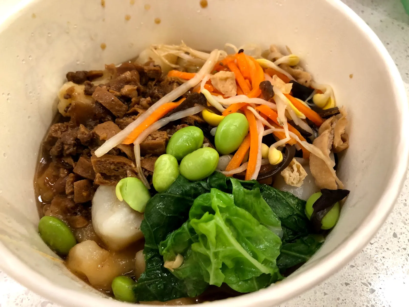 白色碗裡的麵疙瘩湯，湯裡有肉燥、紅蘿蔔絲、毛豆、菇類與一大片青菜
