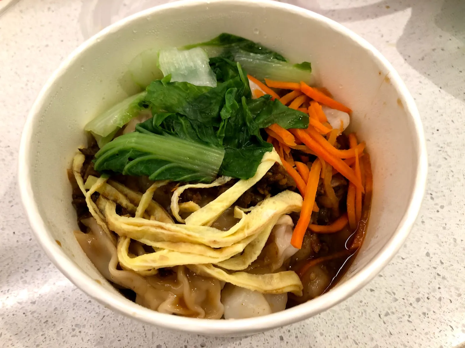 白色碗裡的乾麵疙瘩，寬扁的麵疙瘩上鋪著青菜與紅蘿蔔絲，碗底是紅色的醬汁