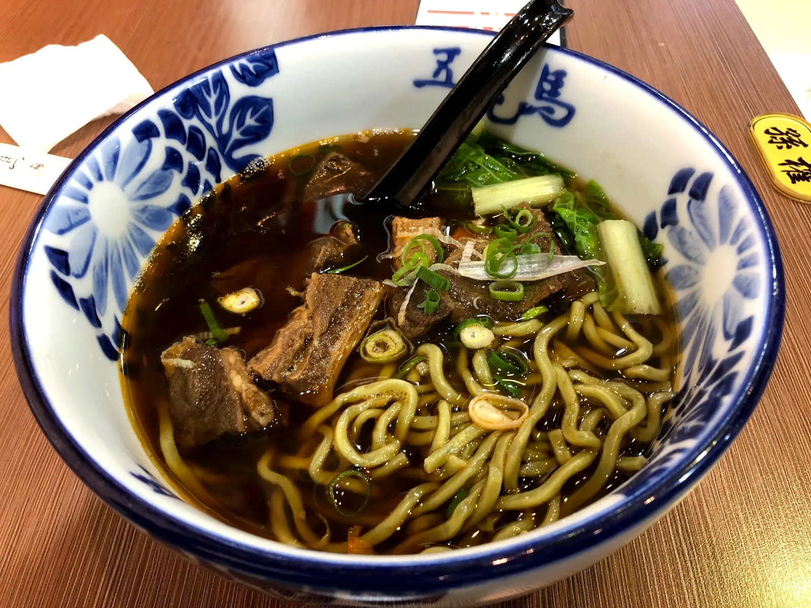 藍白花紋的大碗裡是紅燒牛肉麵，湯裡有牛肉塊、青菜與蔥花