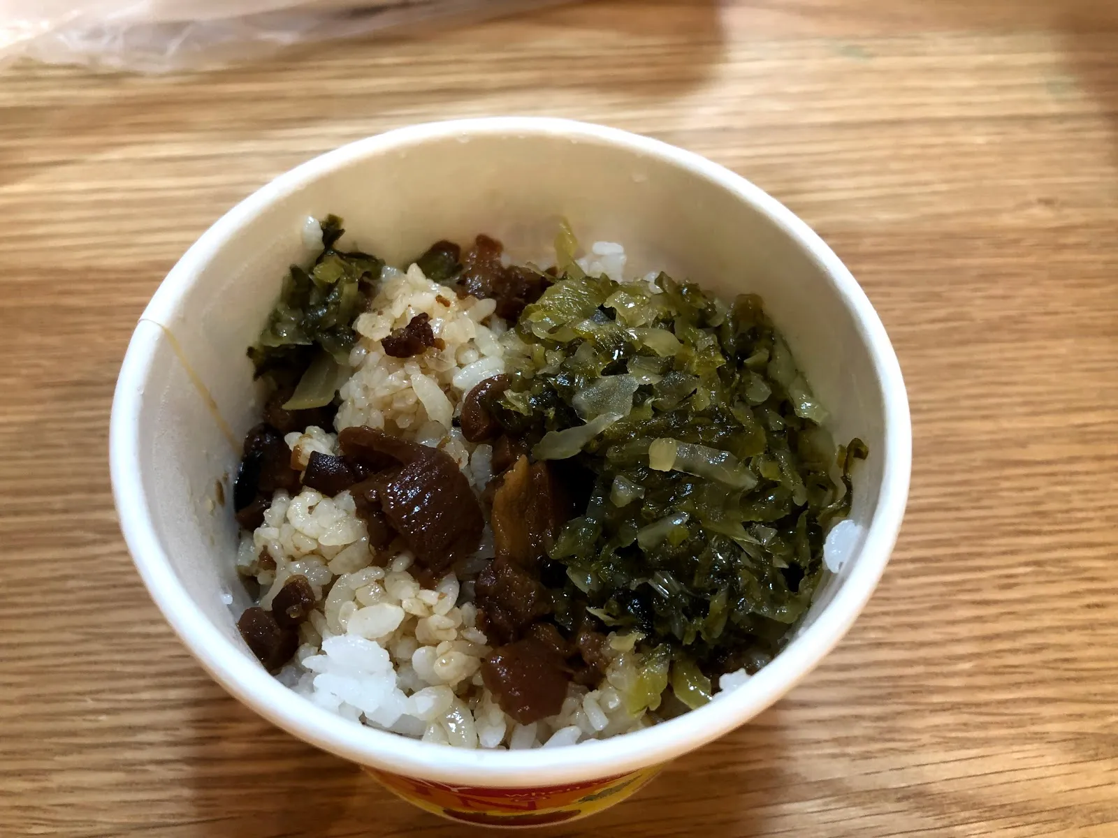紙碗裡的滷肉飯配酸菜，白飯上淋著肉燥，旁邊堆著醃過的酸菜