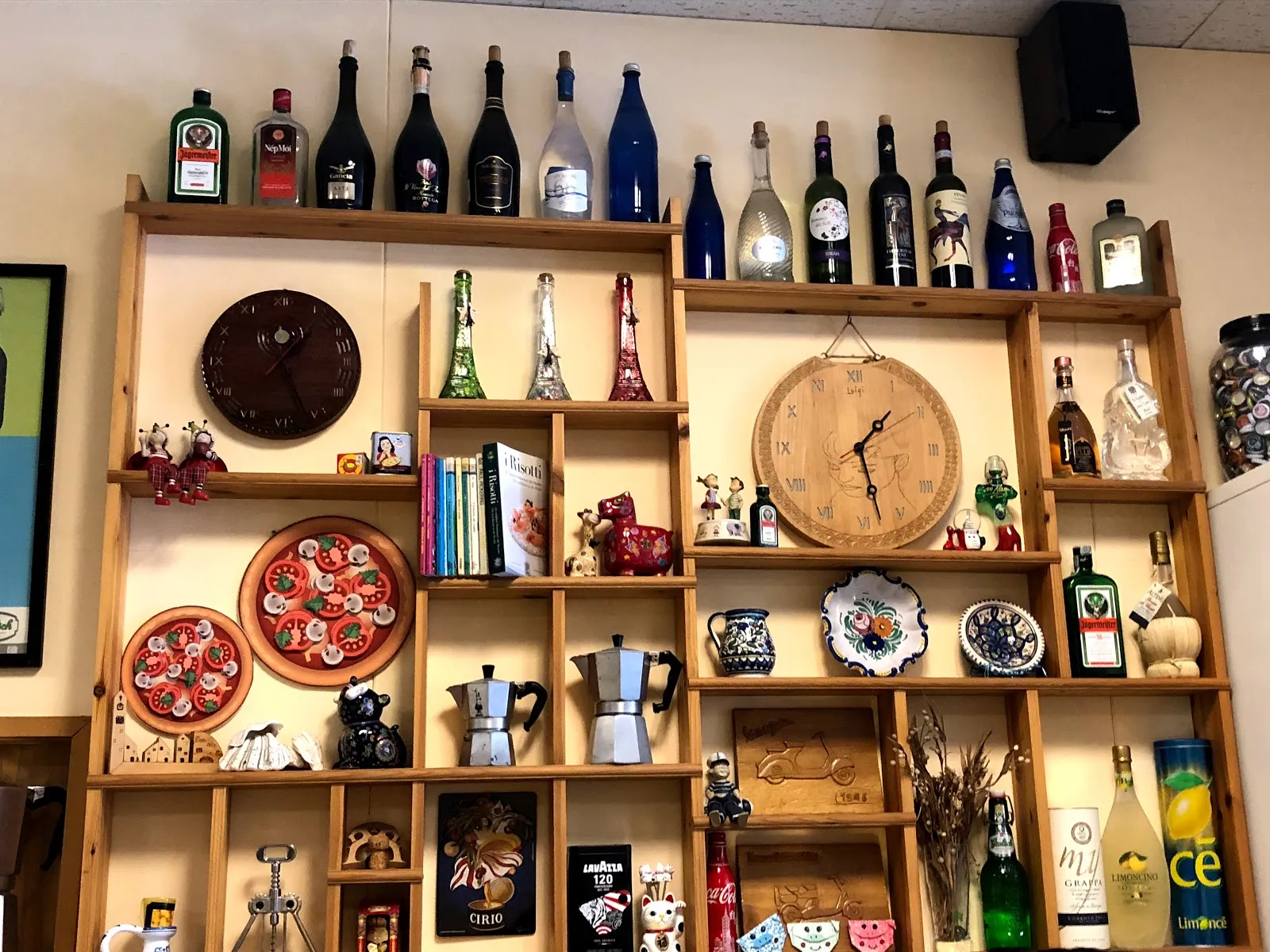 店內的木製格架牆，一格格擺著酒瓶、摩卡壺、彩繪盤與小擺飾，中間掛著兩個時鐘