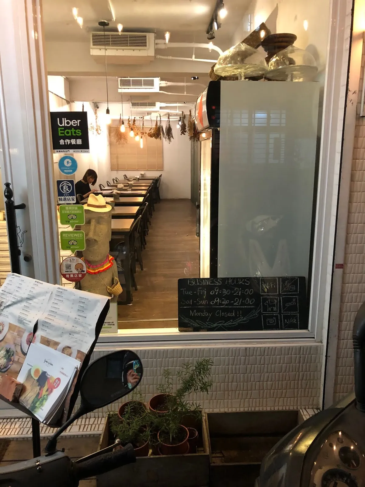從店門口往店內看,狹長的用餐區沿牆排著木桌,玻璃門上貼著 Uber Eats 合作店家的貼紙,門邊立著菜單架與盆栽