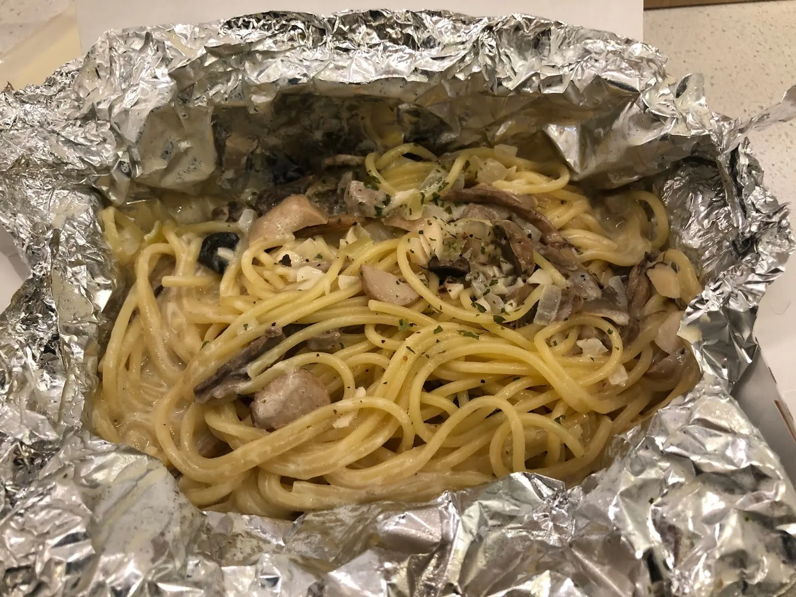 鋁箔盒裡的白醬野菇義大利麵,麵條之間夾著切片的菇類