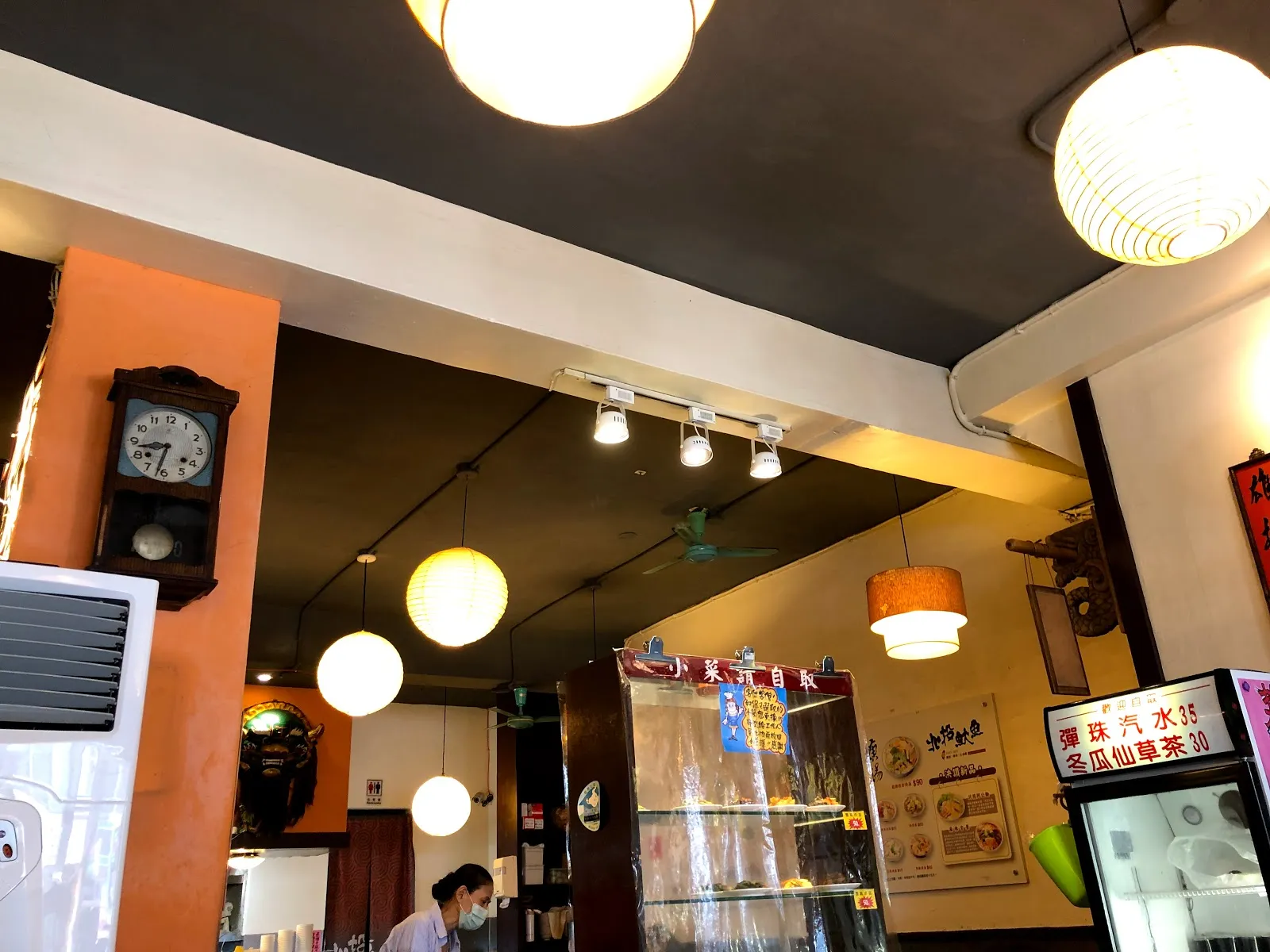 店內另一角，橘色柱子旁掛著老式掛鐘，天花板垂著球形吊燈，後方是點餐櫃檯與飲料冰櫃