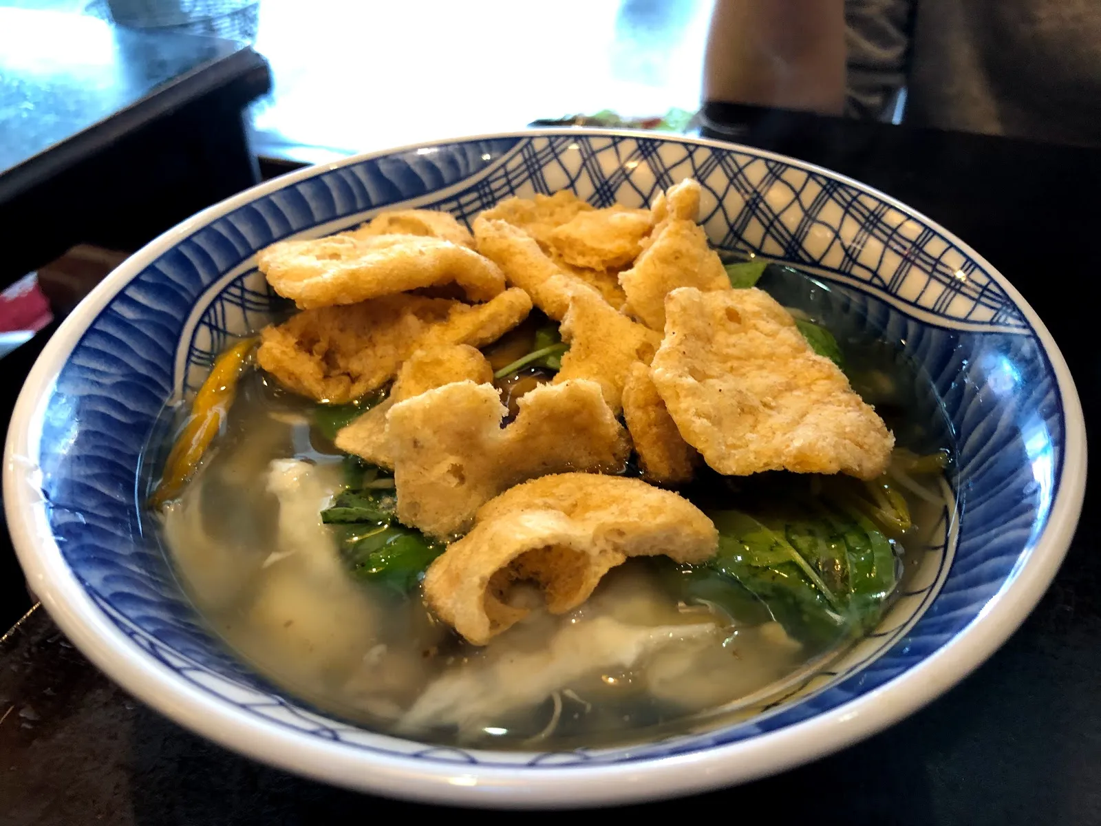 藍白花紋的碗裡是魷魚羹湯，湯裡有青菜與幾塊炸過的豆皮