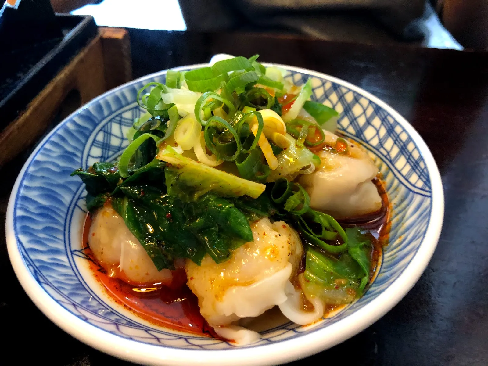 藍白花紋的碗裡是紅油抄手，餛飩上鋪著大量蔥花與青菜，紅油積在碗底