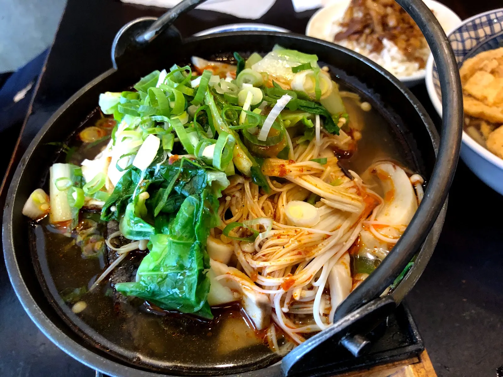 石鍋裡的麻辣湯，湯面鋪滿蔥花、青菜與金針菇