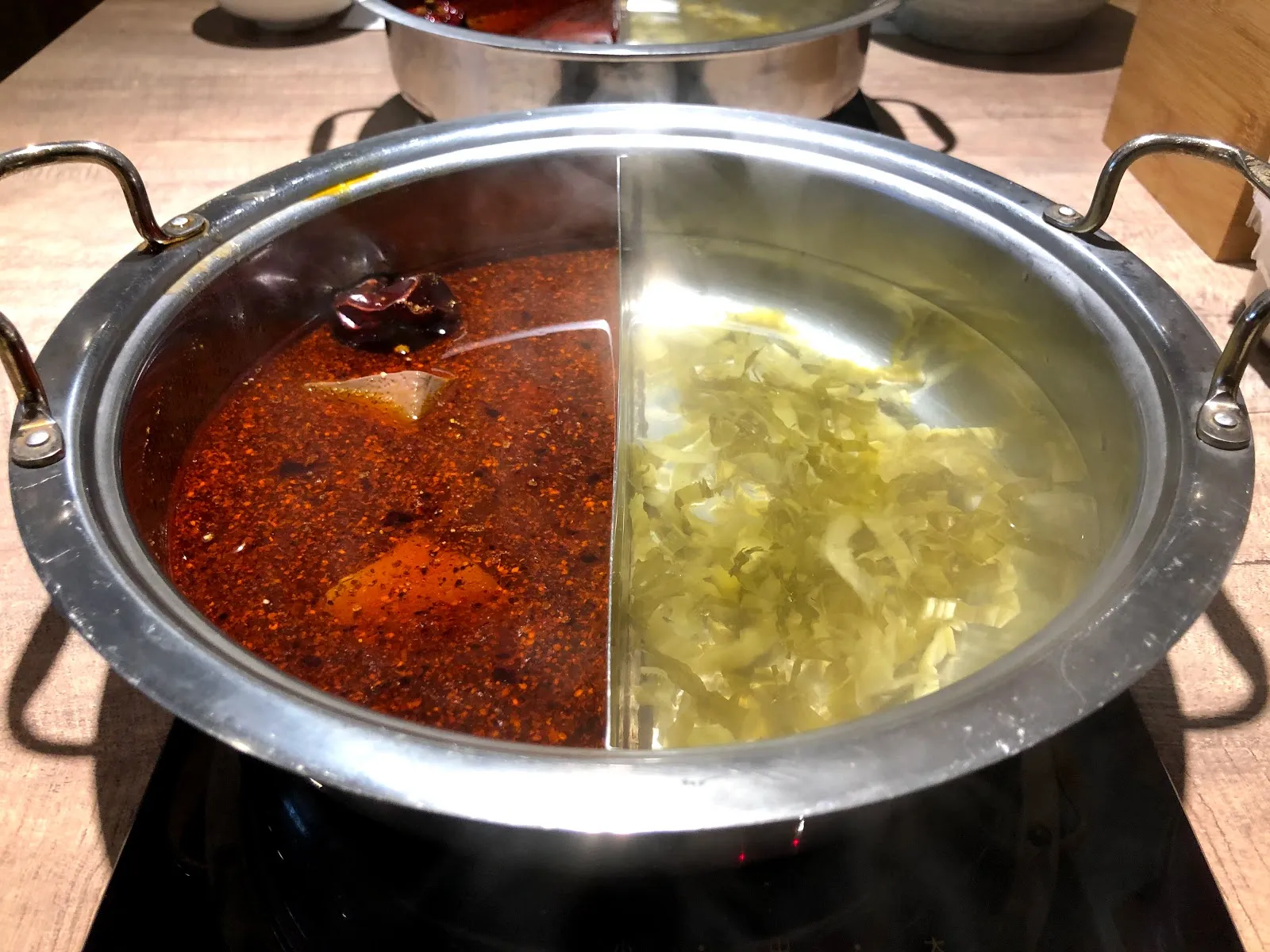 不鏽鋼鴛鴦鍋架在爐上,一邊是浮著花椒與紅油的麻辣湯,一邊是酸菜白湯