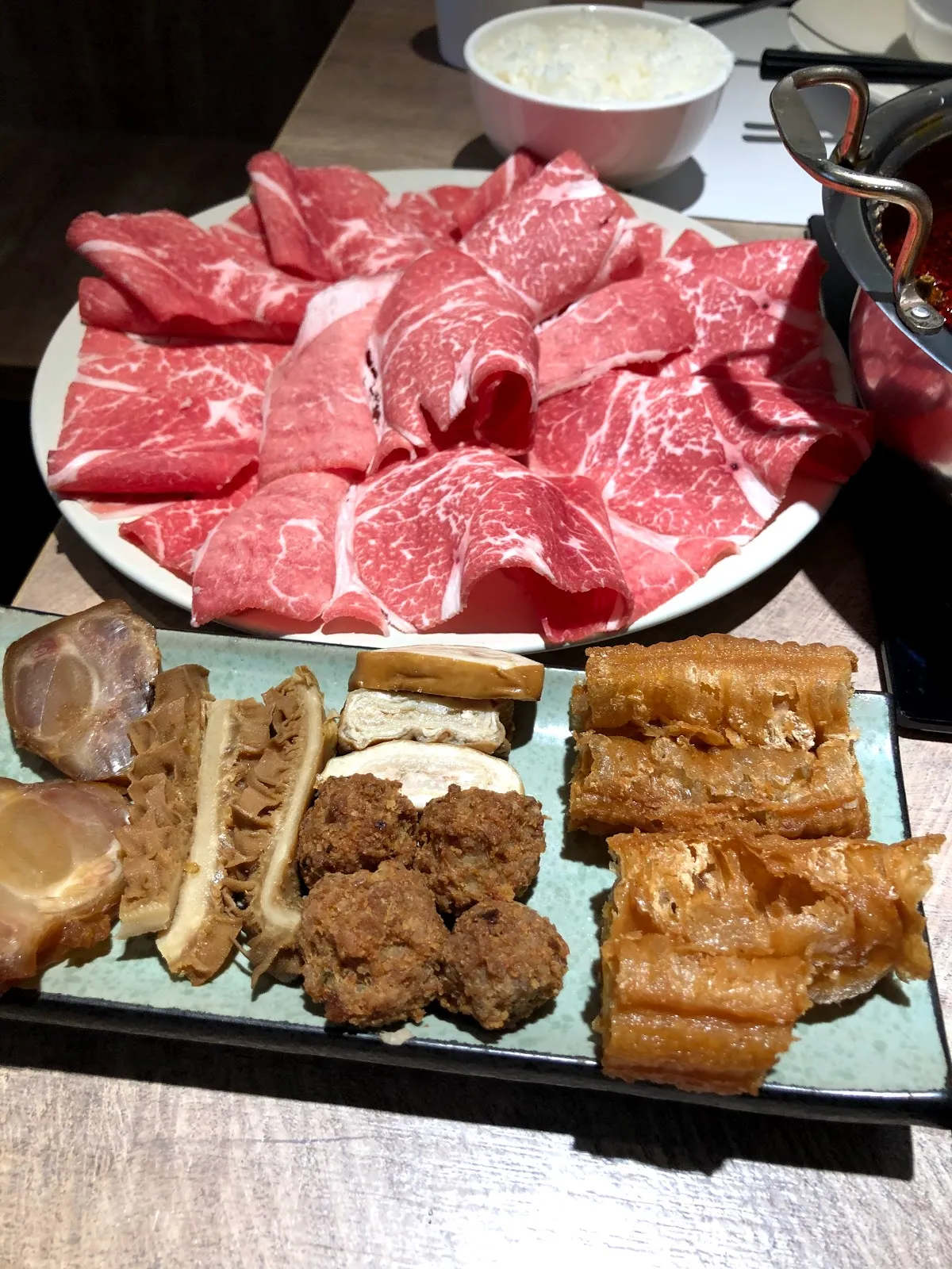 白盤上盛著帶大理石油花的牛肉片,前方長盤是炸豆皮、油條與丸類的拼盤