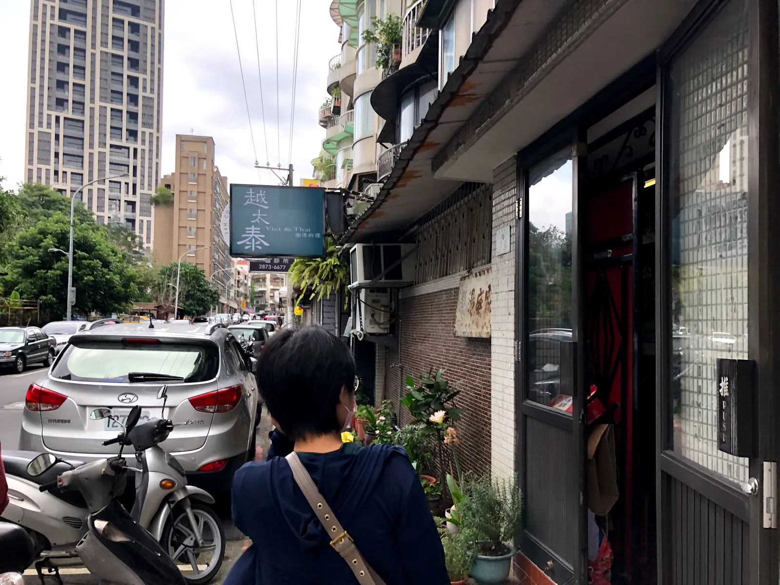 越太泰的店門外街景，深色磚牆門面掛著招牌，路邊停滿汽車與機車，一名行人正走過
