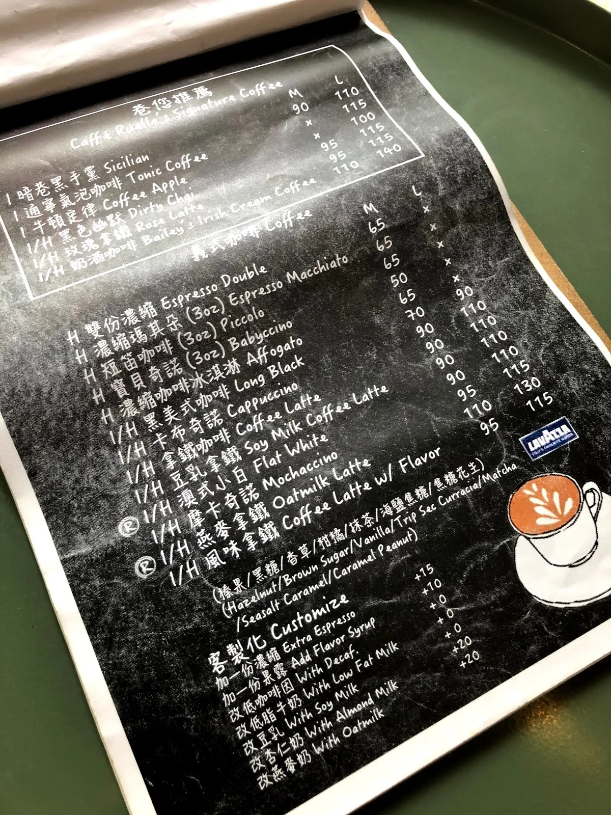 Caffé Ruelle 的咖啡菜單，黑板風格手寫字體，義式濃縮 90、卡布奇諾 110、榛果咖啡拿鐵 130、燕麥拿鐵等，另有客製化加料選項