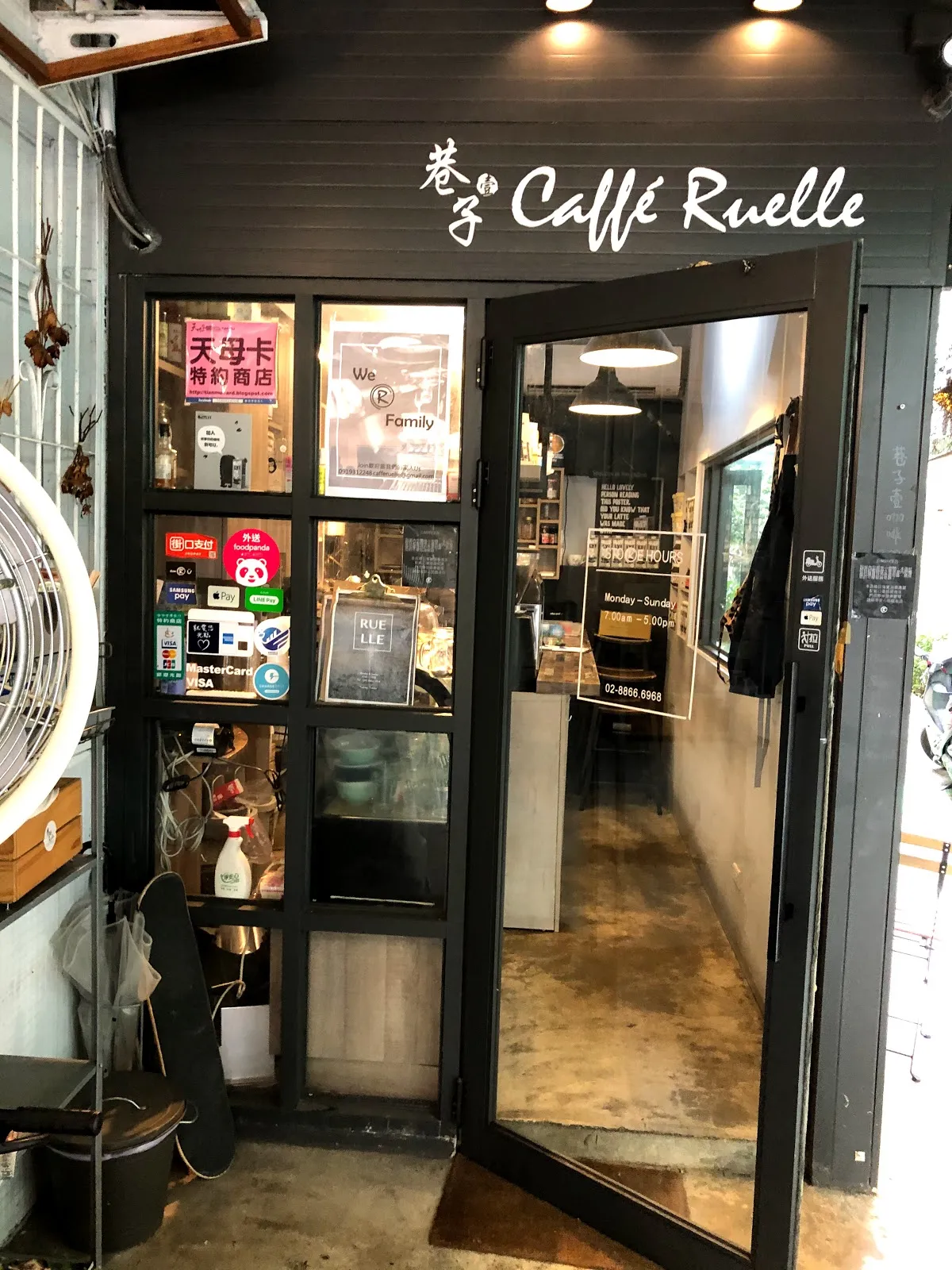 Caffé Ruelle 的店門口，深色木質外牆掛著白色的店名招牌，玻璃門半開看得到店內吧檯