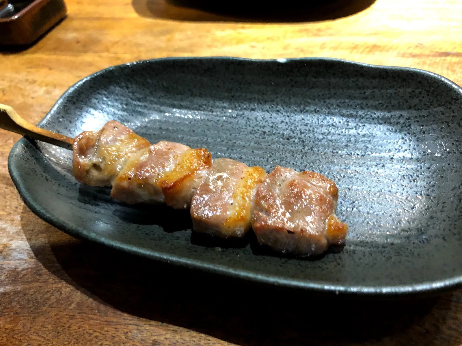 深綠色陶盤上的串燒，三塊帶油花的肉烤到邊緣微焦、表面油亮