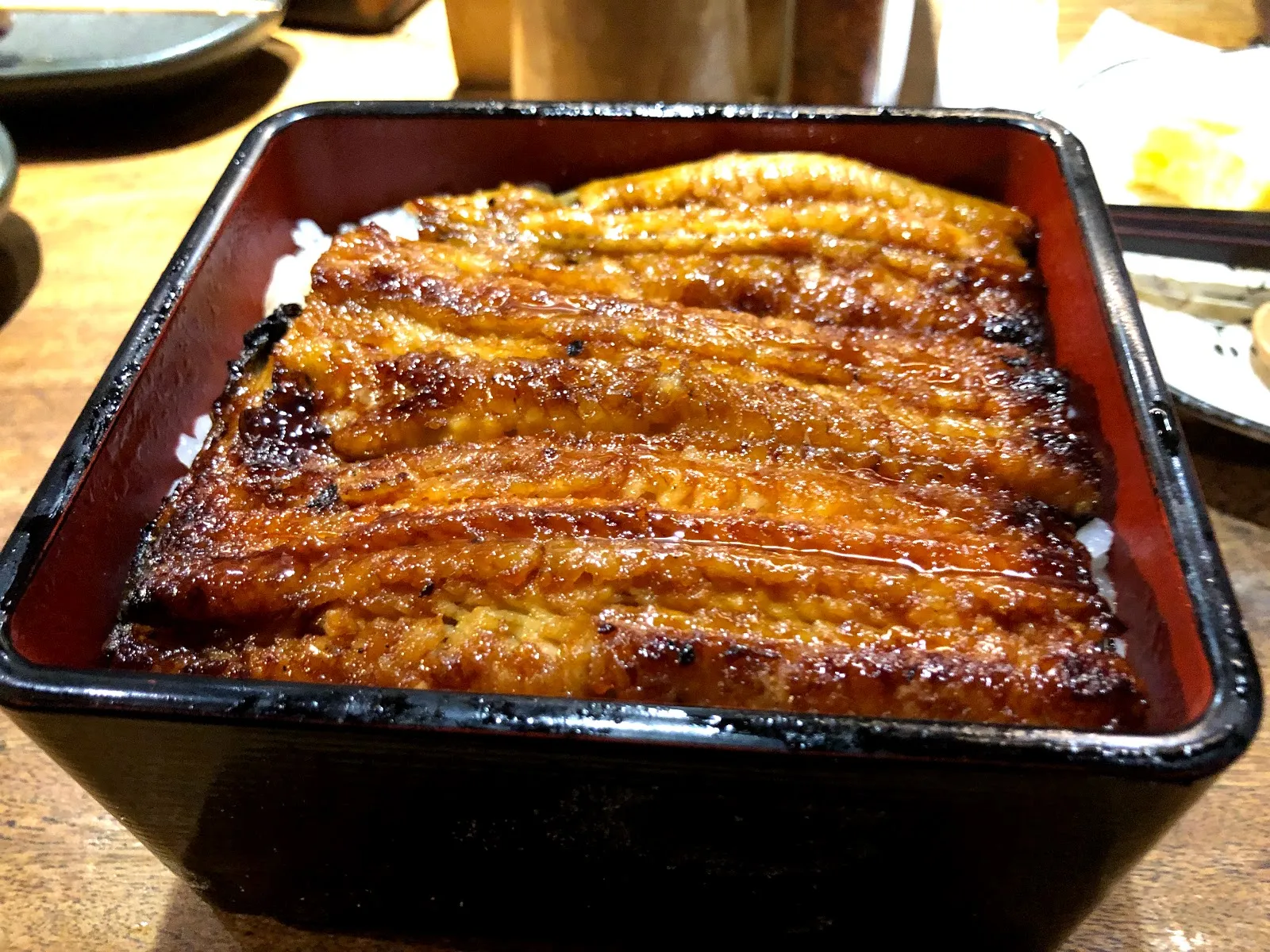 黑色漆器方盒裡的蒲燒鰻魚飯，五條醬色油亮的鰻魚並排鋪滿白飯