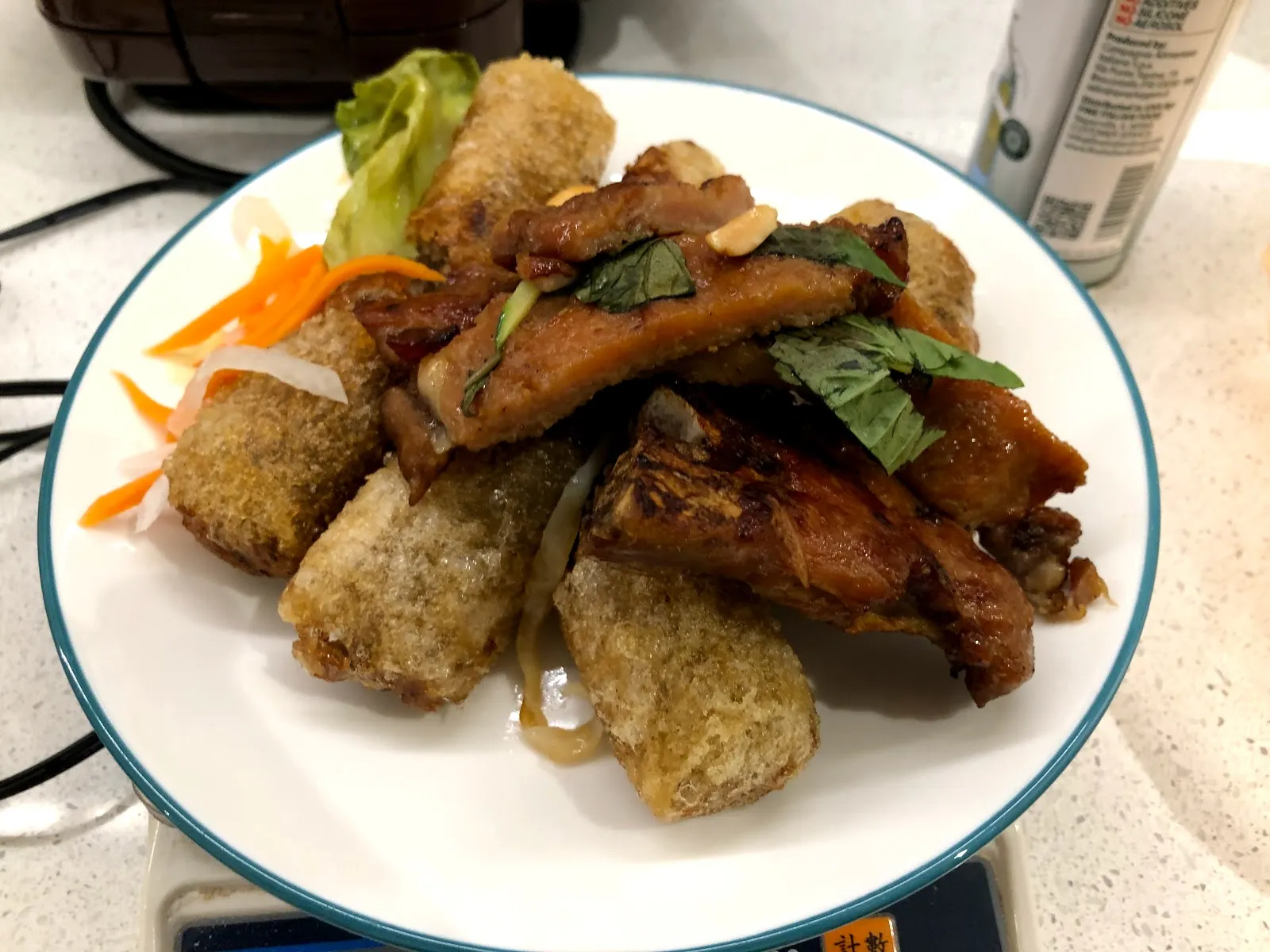 白色圓盤上的越式拼盤，炸春捲與滷得深褐的肉排疊在一起，配上醃蘿蔔絲與九層塔